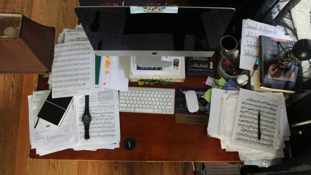 An image of a cluttered desk with a large monitor and paperwork everywhere. Photo by Jesus Hilari.