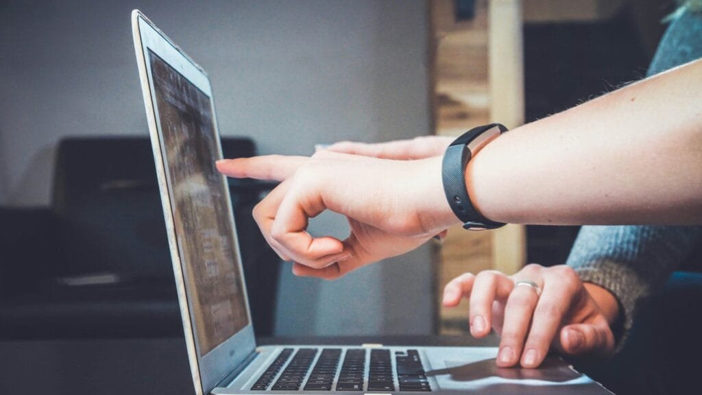 An image that shows a person helping another on a laptop. Representing digital skills training. Photo by John Fip.