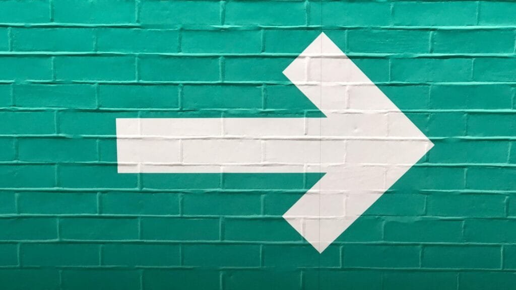 A white arrow on a painted green brick wall. Photo by Nick Fewings.